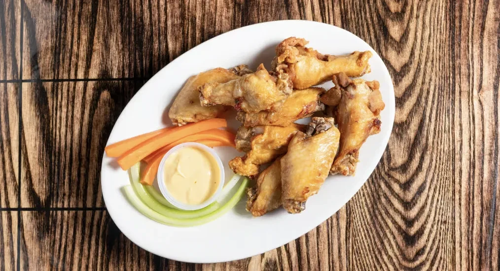 White plate with crispy chicken wings, carrots, celery, and dipping sauce.