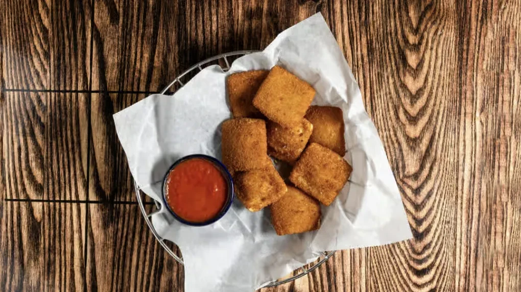 Fried appetizers in a basket with marinara sauce on dark wood.