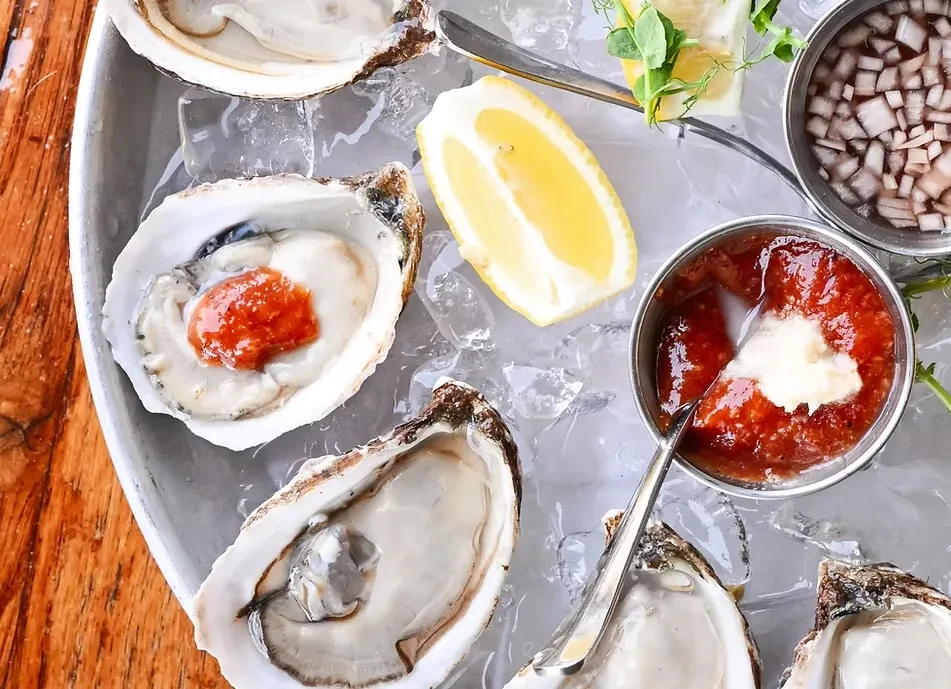Top-down view: Fresh oysters on ice with lemon and condiments.