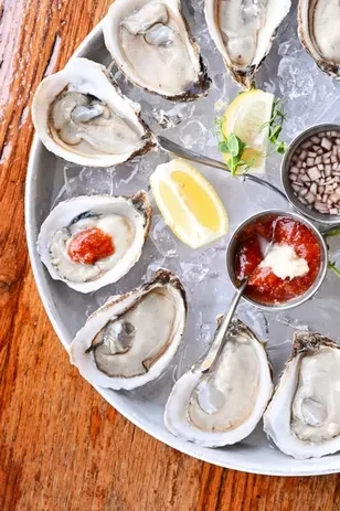 A dozen raw oysters on ice with lemon, cocktail sauce, and mignonette.