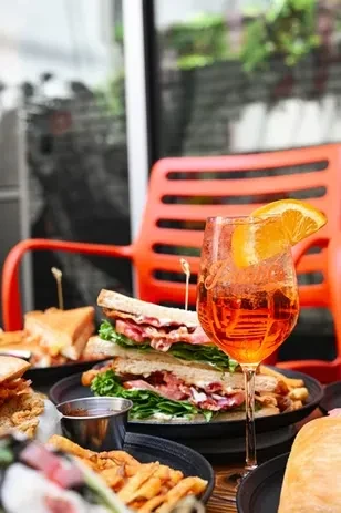 Reddish-orange cocktail, club sandwich, and curly fries on a patio.