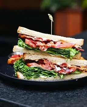Double-decker BLT sandwich, skewered and cut diagonally on a black plate.