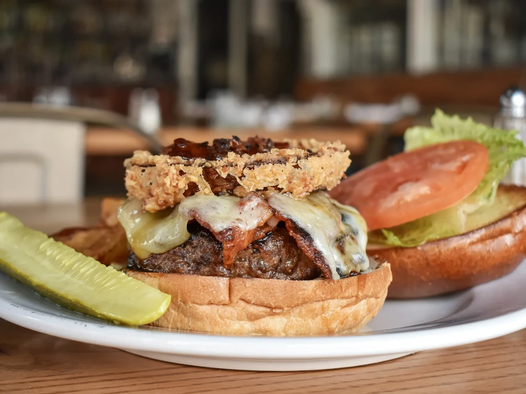 Open-faced gourmet burger with bacon, melted cheese, onion ring, and pickle.