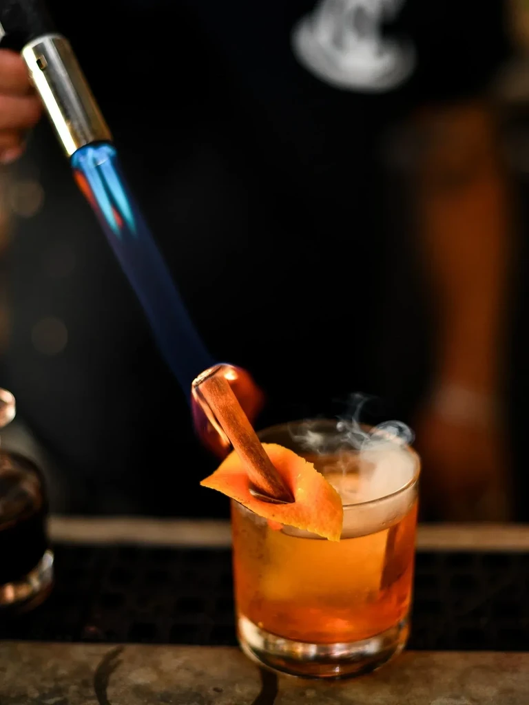 Close-up of cocktail with flaming, smoking cinnamon stick.