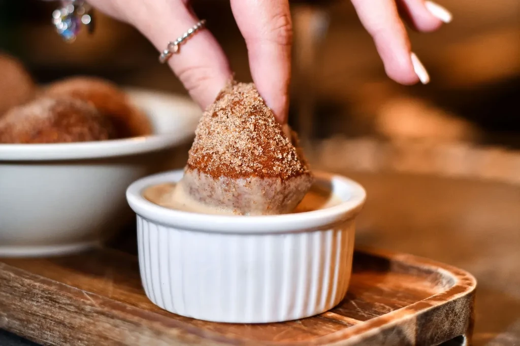 Close-up of hand dipping cinnamon sugar pastry into light brown sauce.