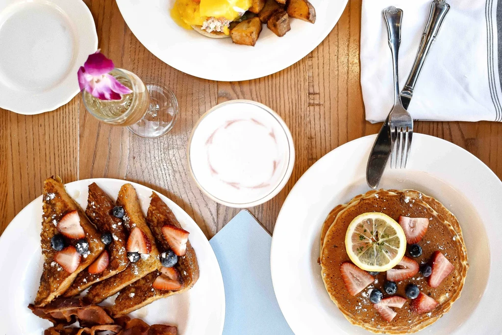 Overhead: French toast, pancakes, Eggs Benedict, and drinks on a table.