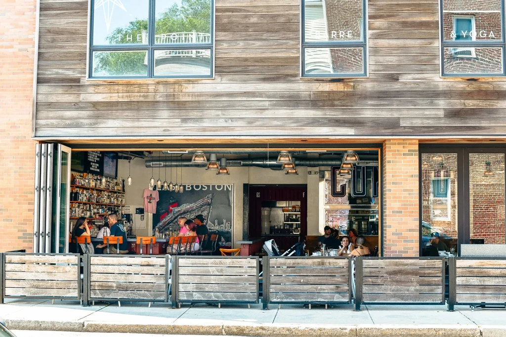Lively urban restaurant with open front, outdoor patio, and "THE BOSTON" sign.