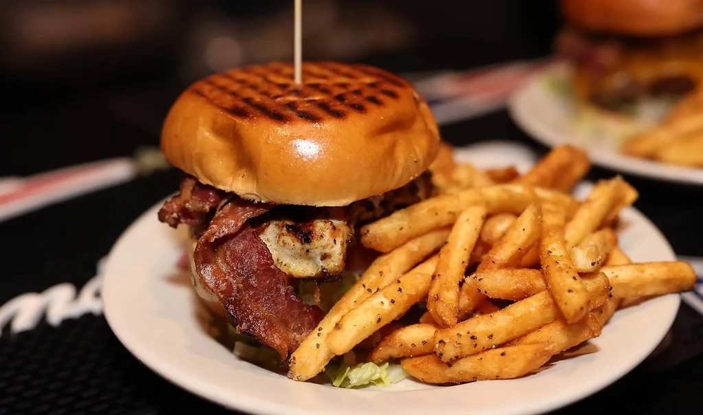 Gourmet burger with bacon, grilled patty, lettuce, and seasoned fries.