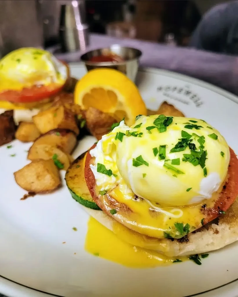 Eggs Benedict with hollandaise, roasted potatoes, herbs, and lemon.