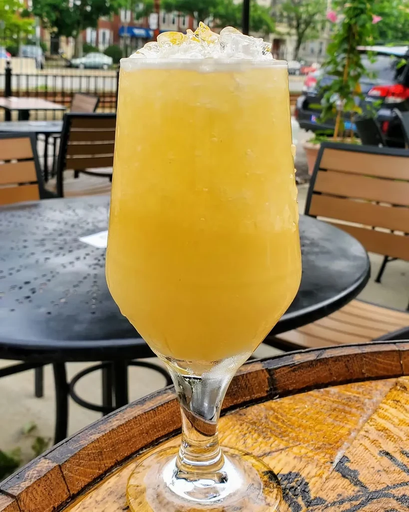 Yellow frozen drink with ice and garnish on a wooden table outdoors.