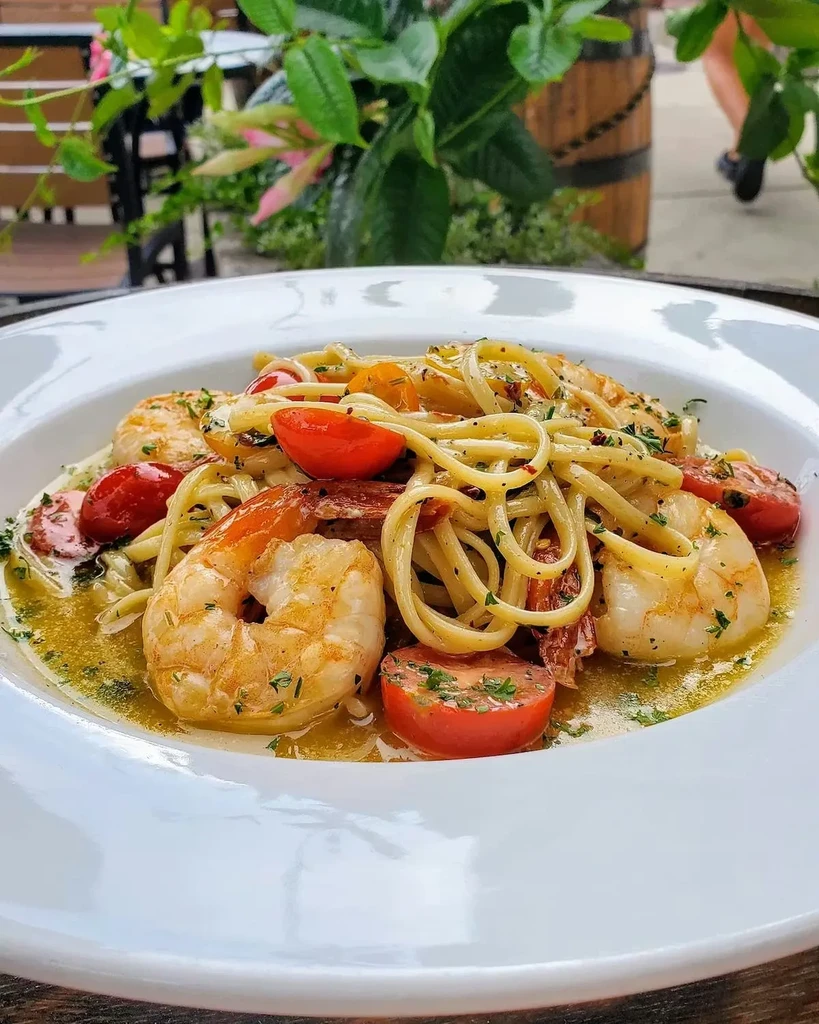 Vibrant shrimp pasta with cherry tomatoes and herbs, outdoor setting.