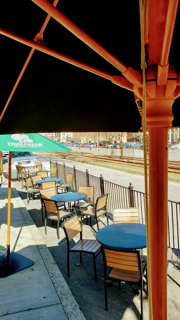 Sunny outdoor restaurant patio with umbrellas, tables, and street with tracks.