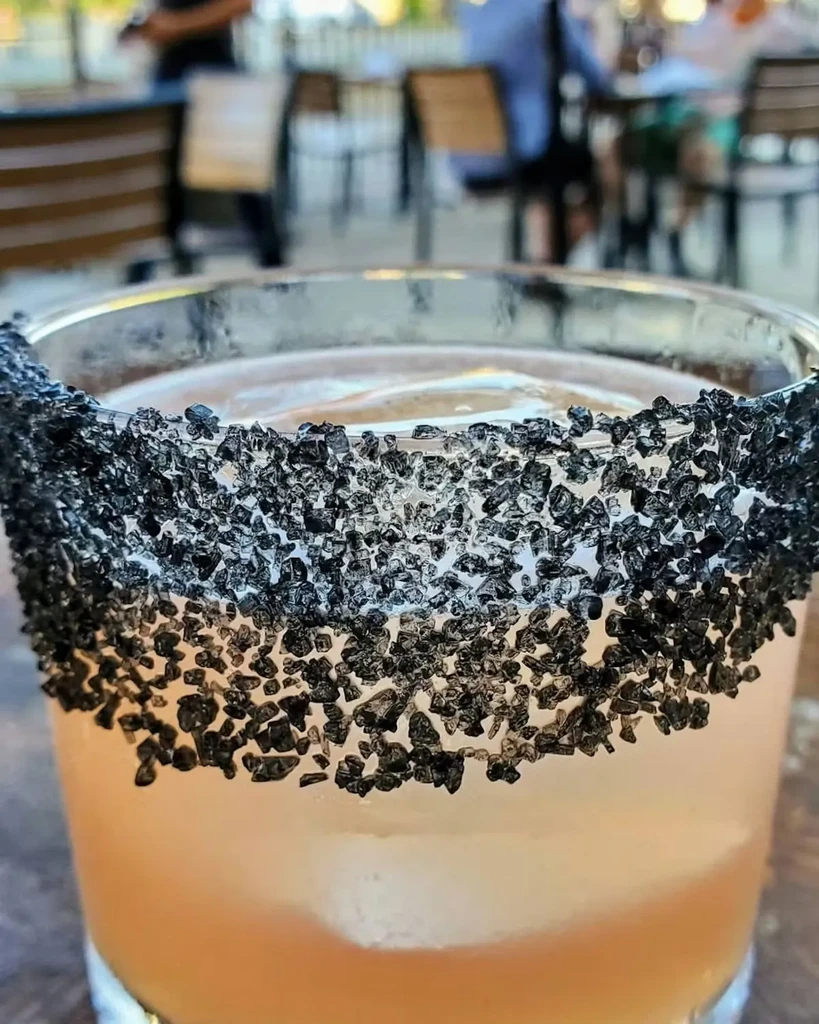 Amber drink in a glass, rim coated with coarse black crystals.