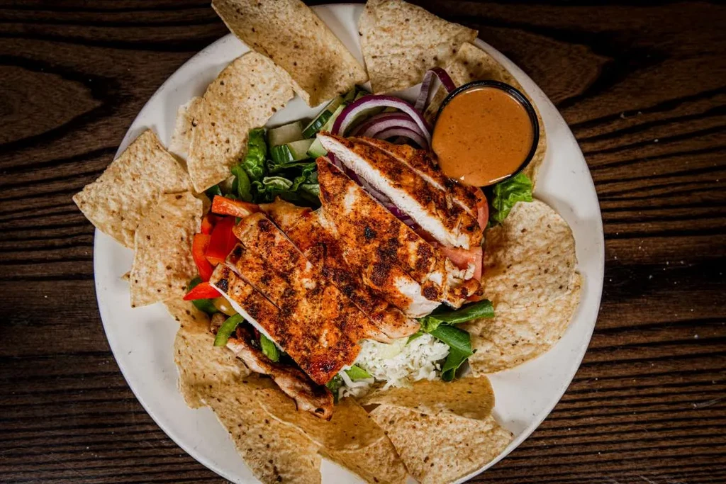 Red-spiced grilled chicken salad with chips and sauce on wood.