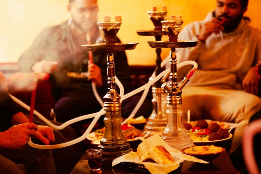 Cozy interior with shisha pipes, food, and blurred people smoking.
