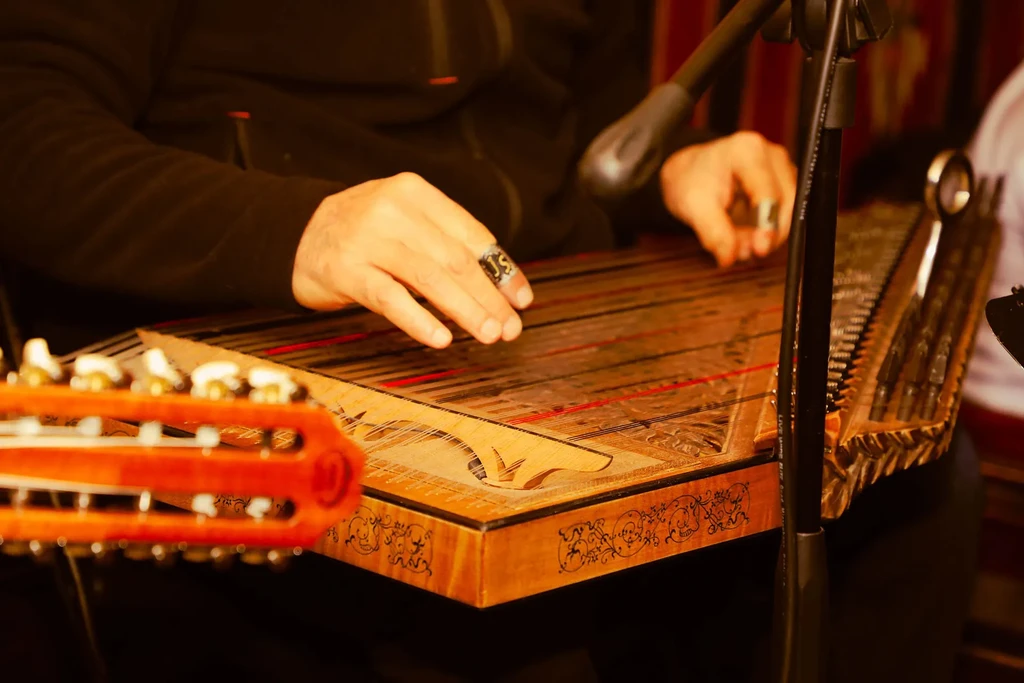 Close-up: Musician's hands play an intricately carved wooden zither.