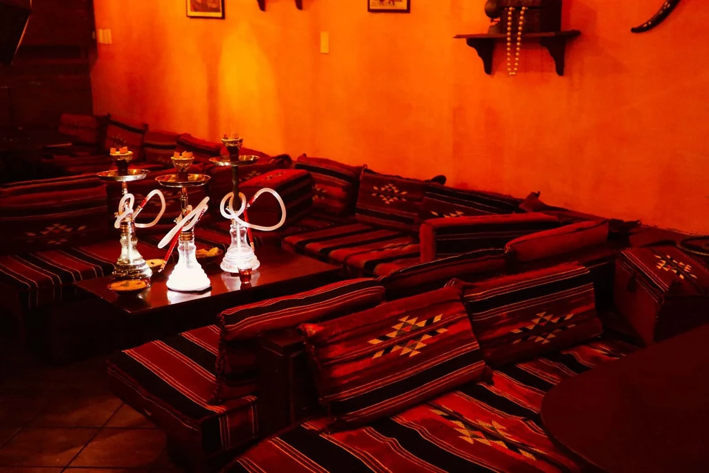 Cozy, dim, orange-red shisha lounge interior with three prominent hookahs.