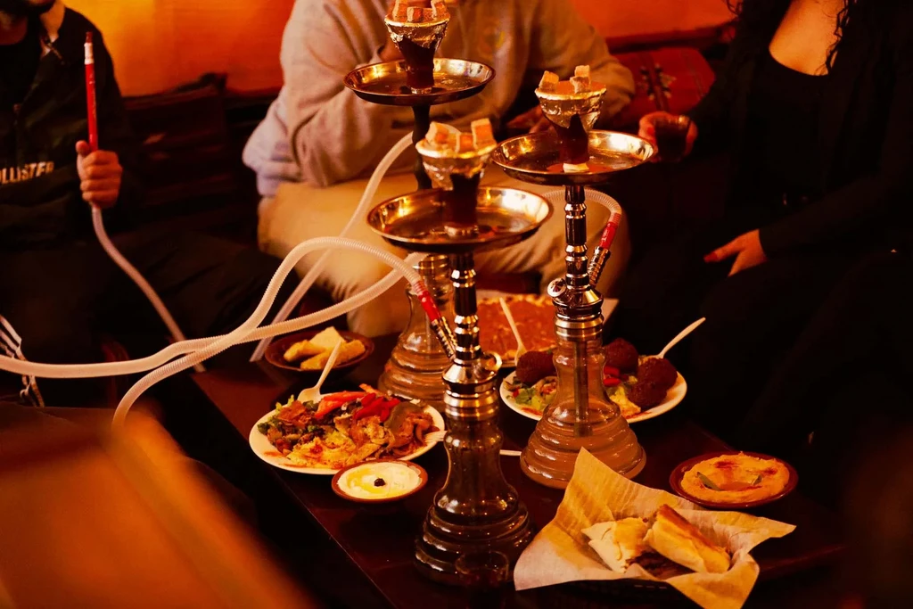 Ornate hookahs and various Middle Eastern dishes shared by people.