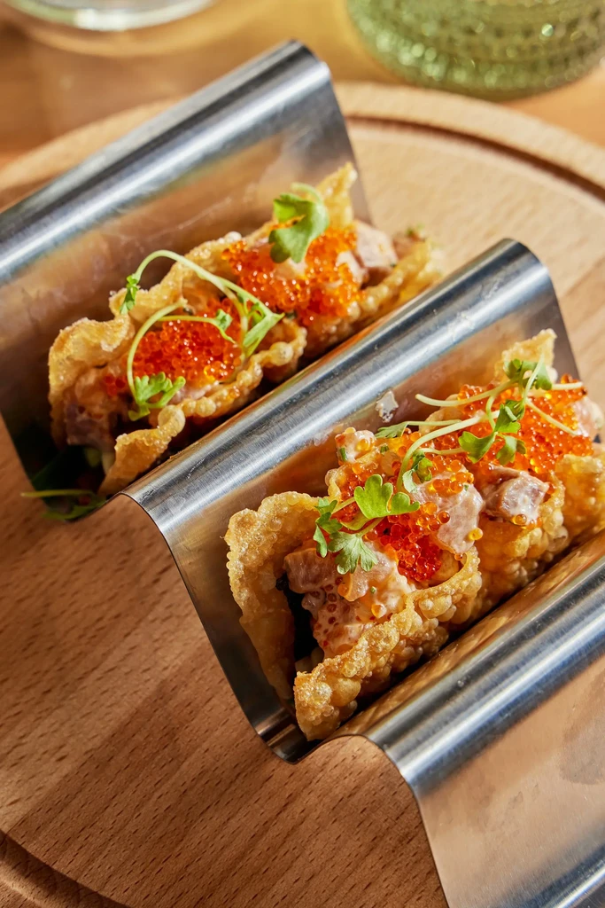 Two crispy appetizers topped with roe and microgreens in silver holders.