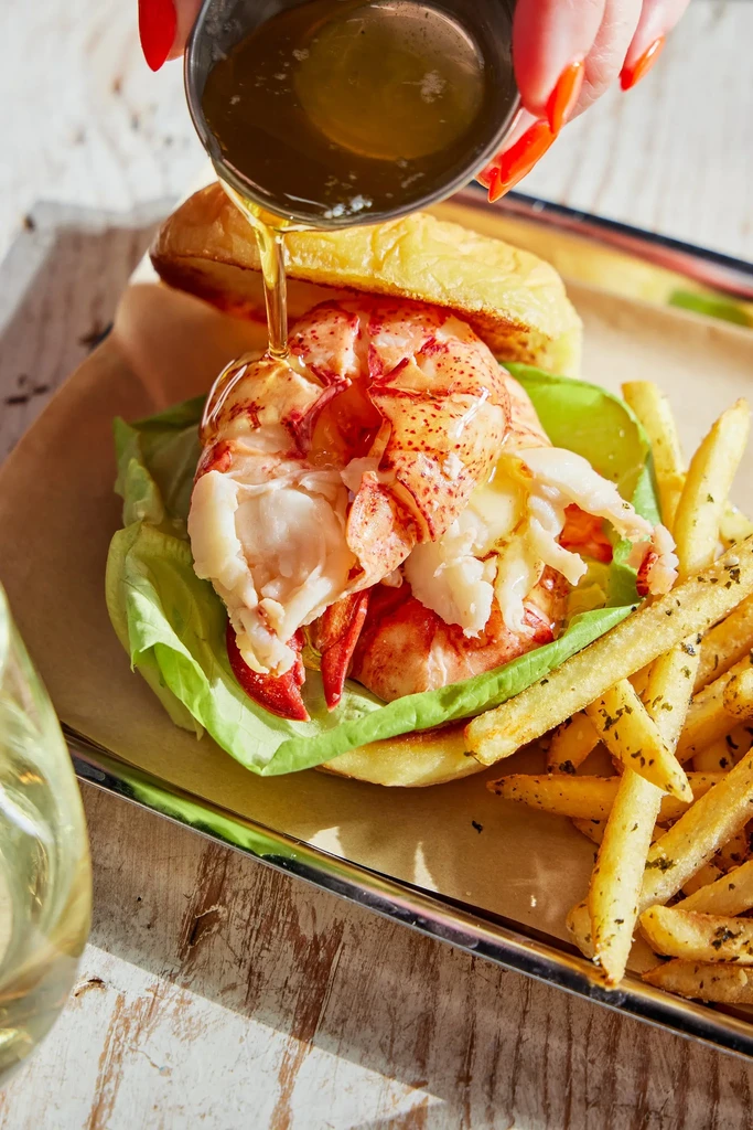 Close-up of a lobster roll with fries, butter poured over the lobster.