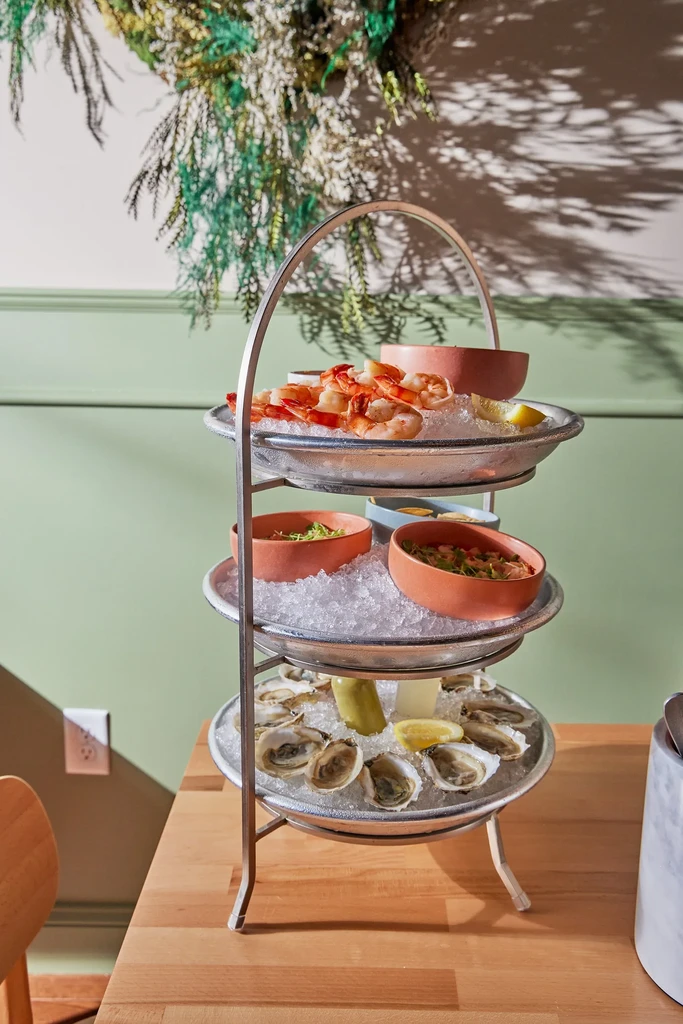 Silver three-tiered seafood tower with shrimp, oysters, lemons, and sauces.