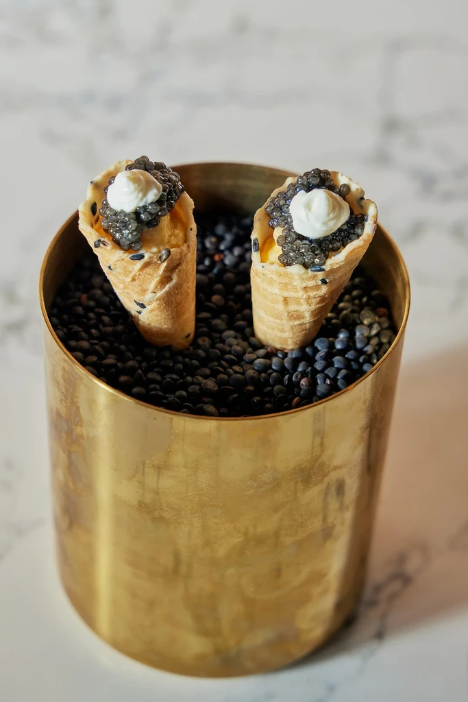 Two savory cones with caviar and cream in a brass container.