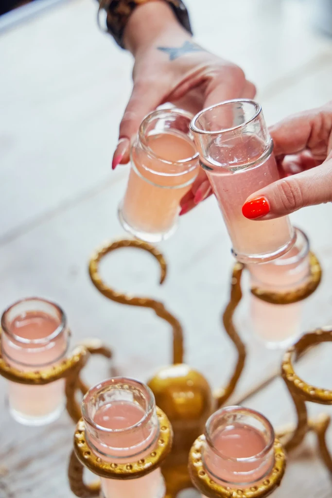 Two hands toast pink drinks from a golden octopus stand.