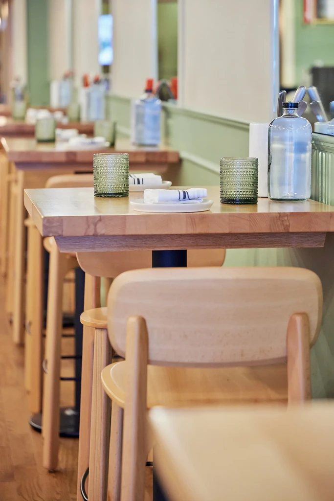 Neatly set high-top wooden tables and chairs inside a modern restaurant.