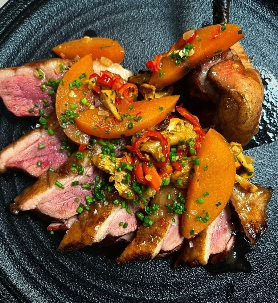 Plated duck breast with glossy sauce, squash, mushrooms, and chives.
