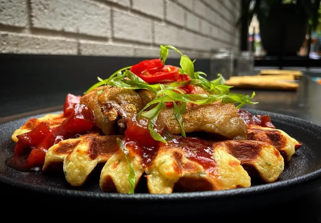 Golden waffles topped with fried chicken, sauce, green herbs, and chilies.