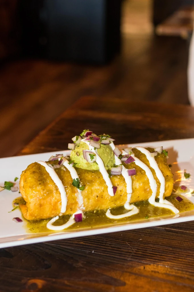 Mexican dish with green salsa, white crema, guacamole, dark table.