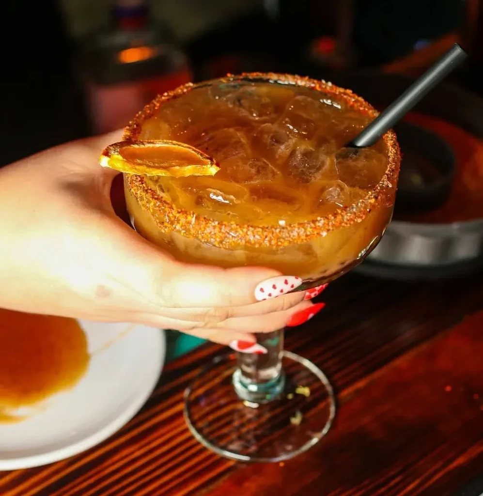 Hand holding dark amber cocktail in salt-rimmed margarita glass.
