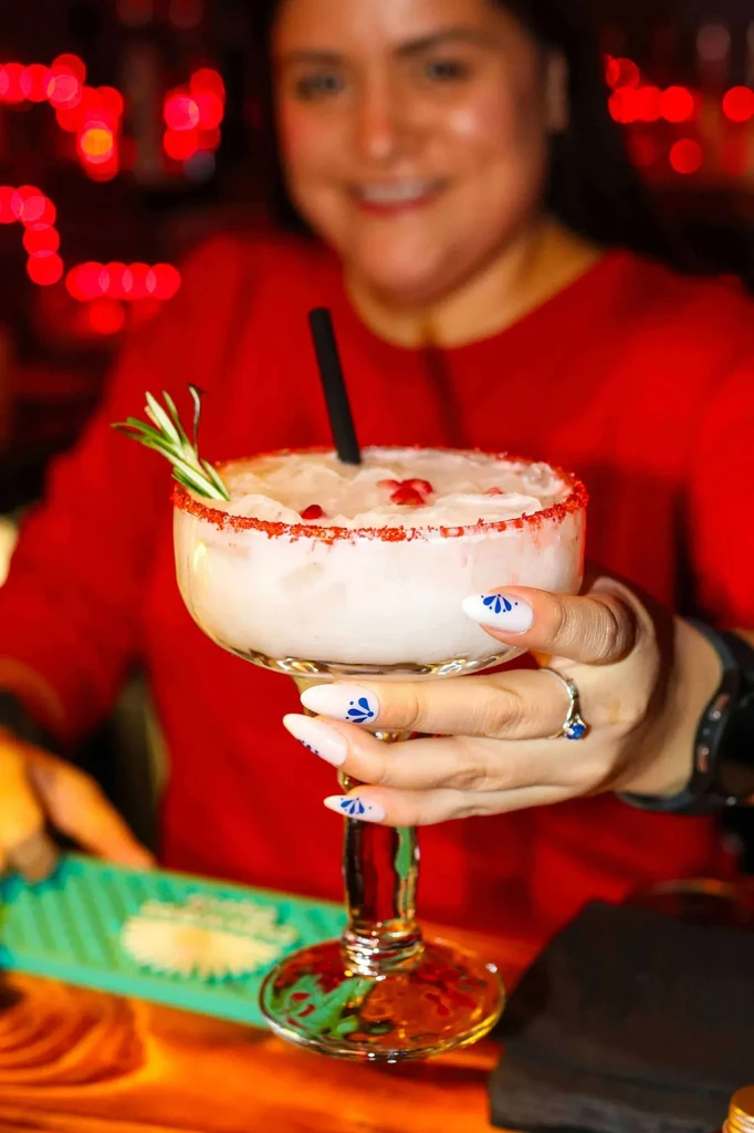 Hand holding a festive creamy cocktail with rosemary and pomegranate.
