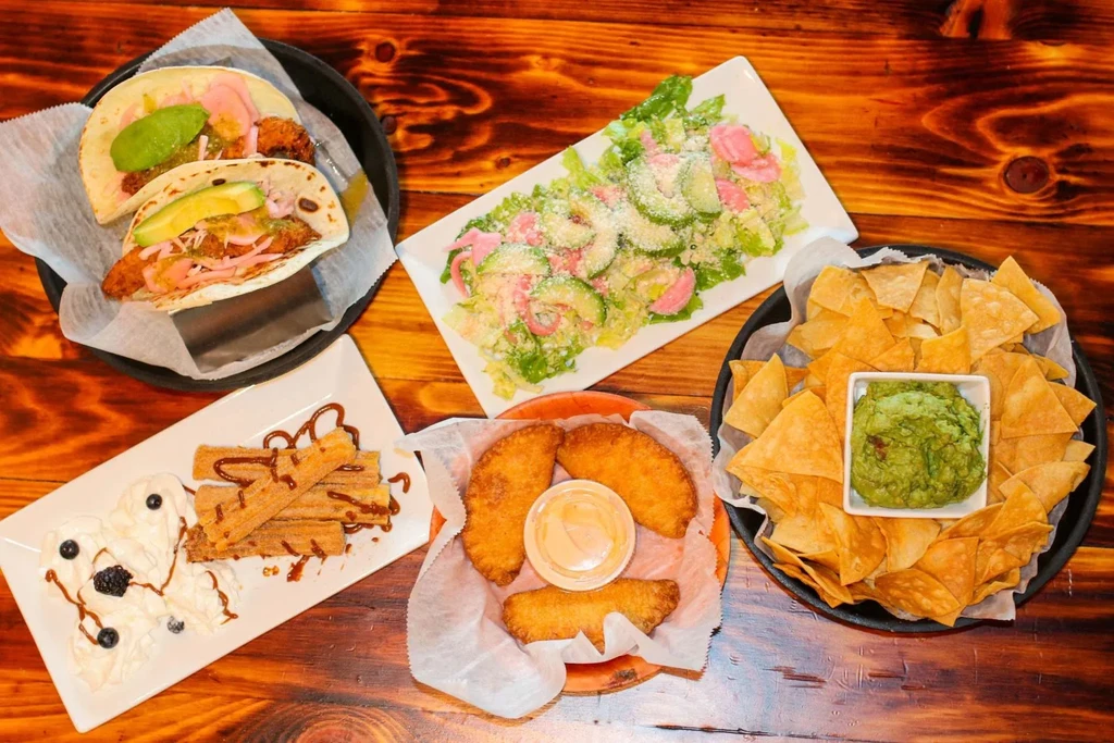 Overhead view: Diverse Latin American dishes, tacos, salad, chips, churros, rustic table.