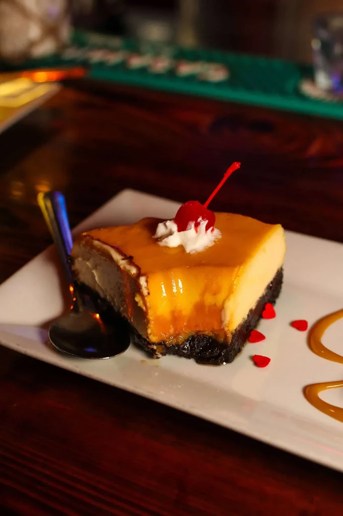 A slice of caramel-topped dessert with whipped cream, cherry, and sprinkles.