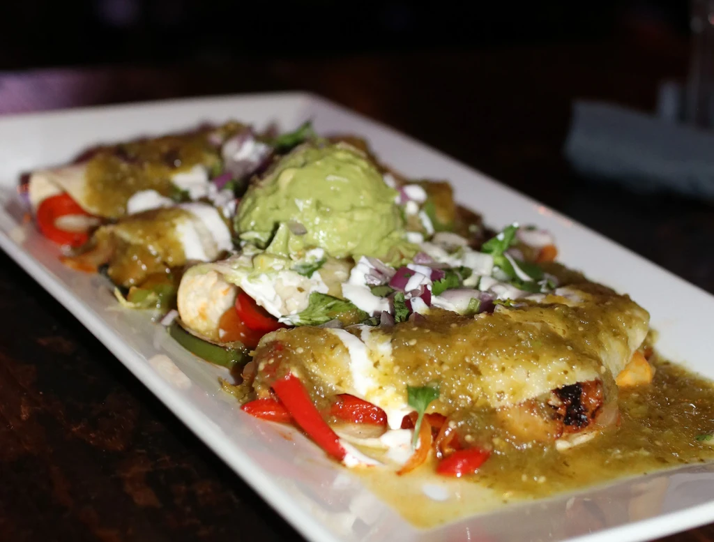 Close-up of enchiladas with green salsa, guacamole, sour cream, and cilantro.
