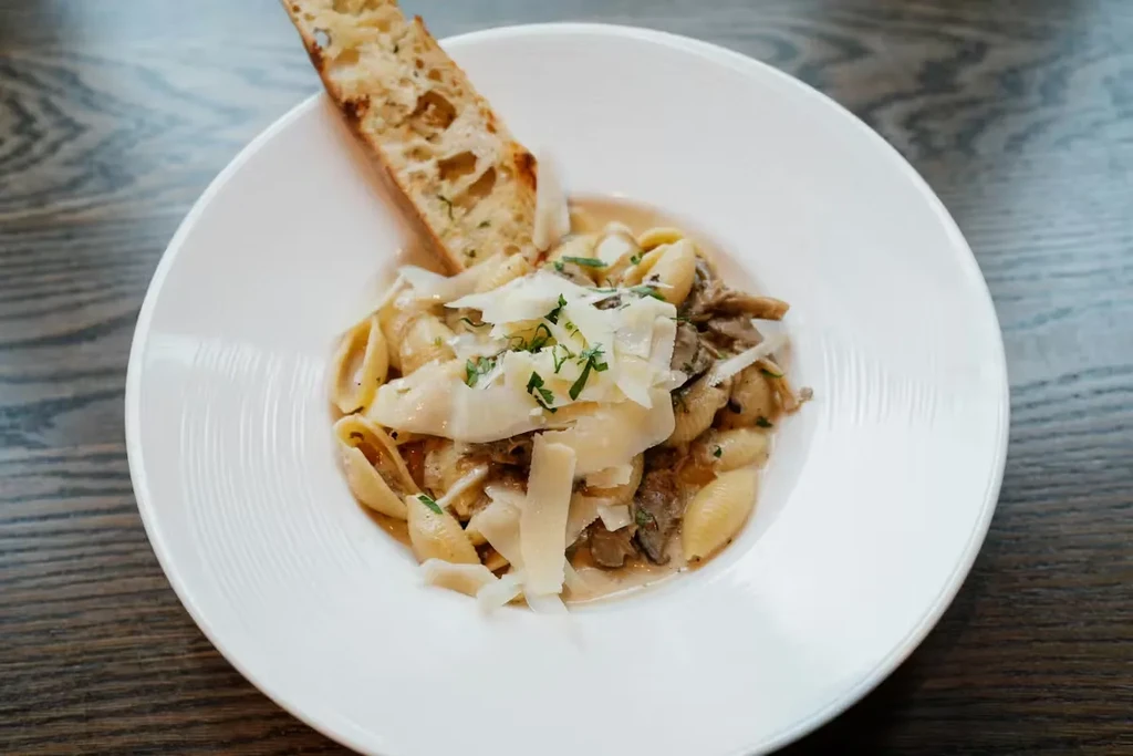 Bowl of creamy shell pasta, parmesan, herbs, mushrooms, and toast.