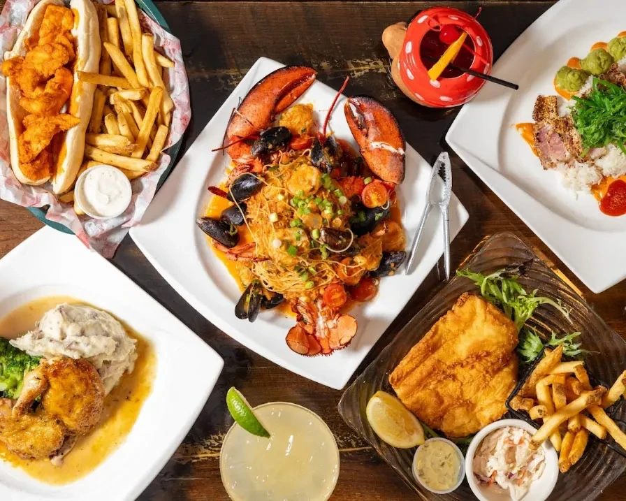 Overhead view of multiple diverse dishes and cocktails on a wooden table.