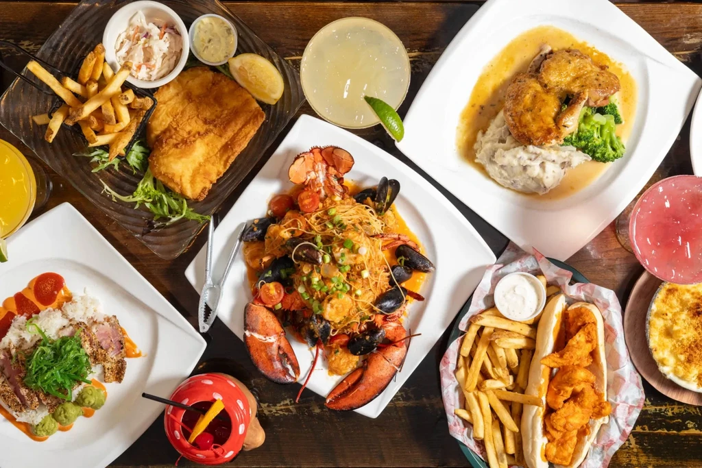 Overhead flat lay of diverse seafood, chicken, sides, and cocktails.