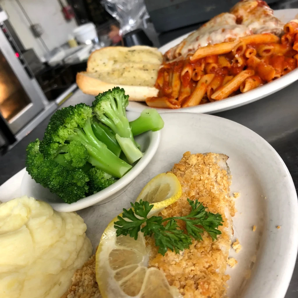 Close-up of two plates: breaded fish, mashed potatoes, and penne pasta.