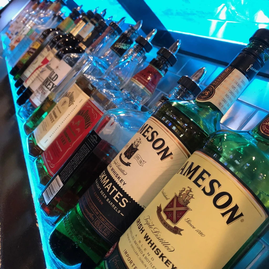 Blue LED backlit liquor bottles line a modern bar shelf.
