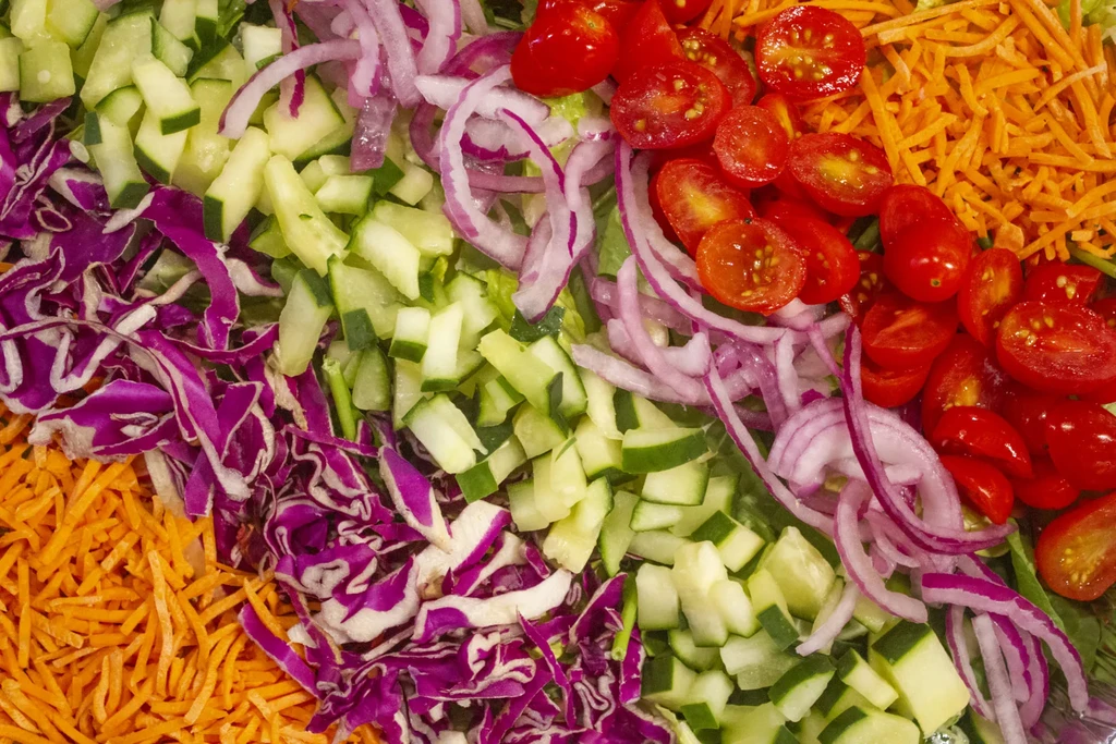 Fresh carrots, cabbage, cucumbers, onions, tomatoes in distinct sections.