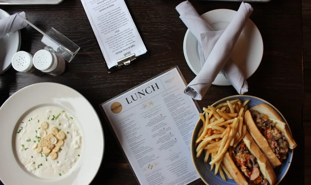 Restaurant table with clam chowder, sandwiches, french fries, and menus.