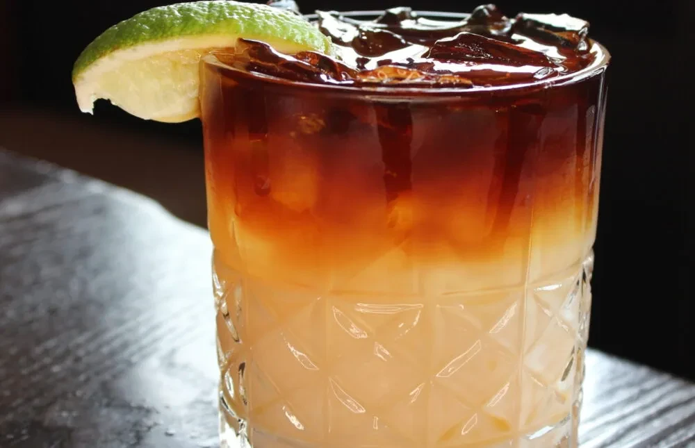 Layered amber and cream drink in a diamond-cut glass, lime garnish.