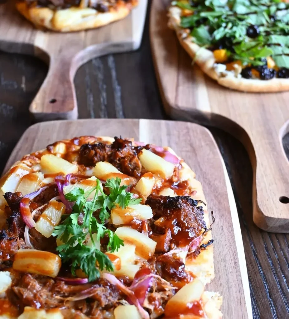 Three gourmet pizzas on wooden boards, one with pulled meat and pineapple.