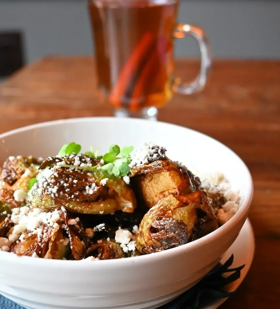 Bowl of caramelized brussels sprouts with crumbled cheese and microgreens.