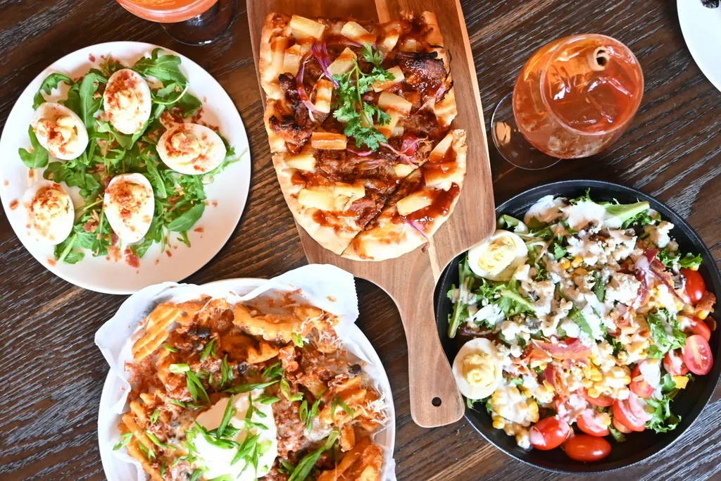 Assortment of deviled eggs, flatbread, loaded fries, salad, and cocktails.