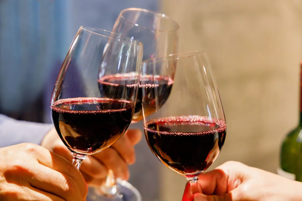 Three red wine glasses clinking together, held by hands.