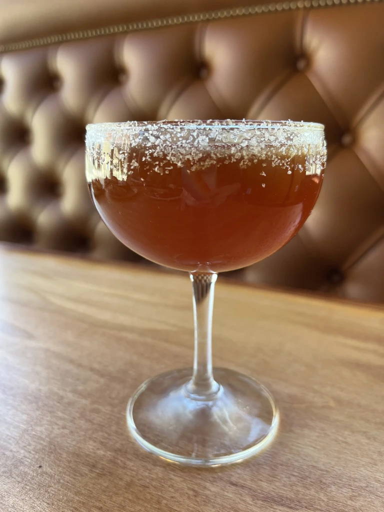 Amber cocktail in a crystal-rimmed coupe on a wooden table.