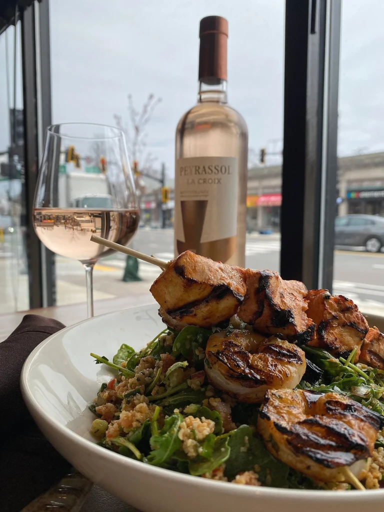 Close-up of salad with grilled shrimp, skewer, rosé wine outdoors.